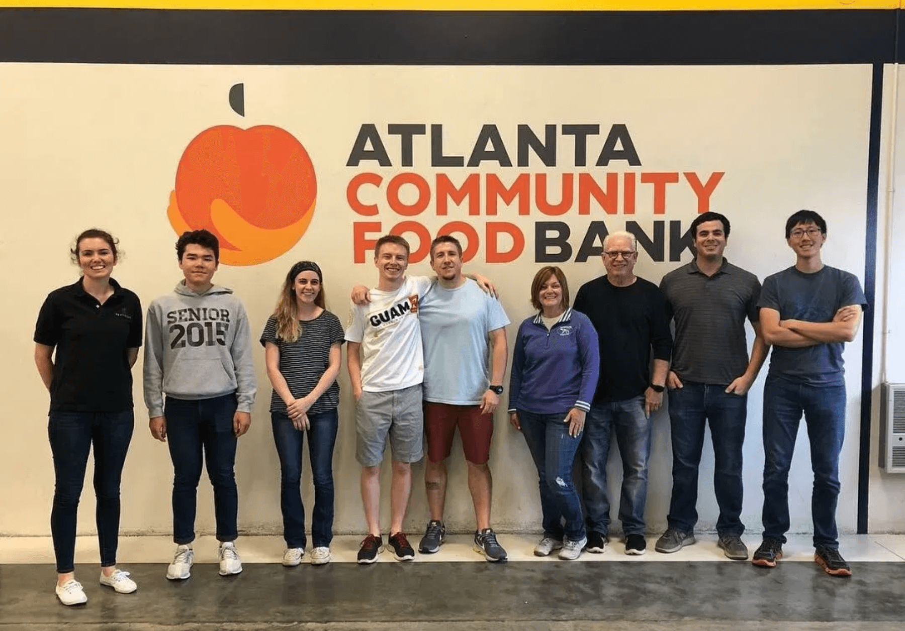 9 staff and volunteers at the Atlanta Community Food Bank posing in front of a sign with the organization's logo.