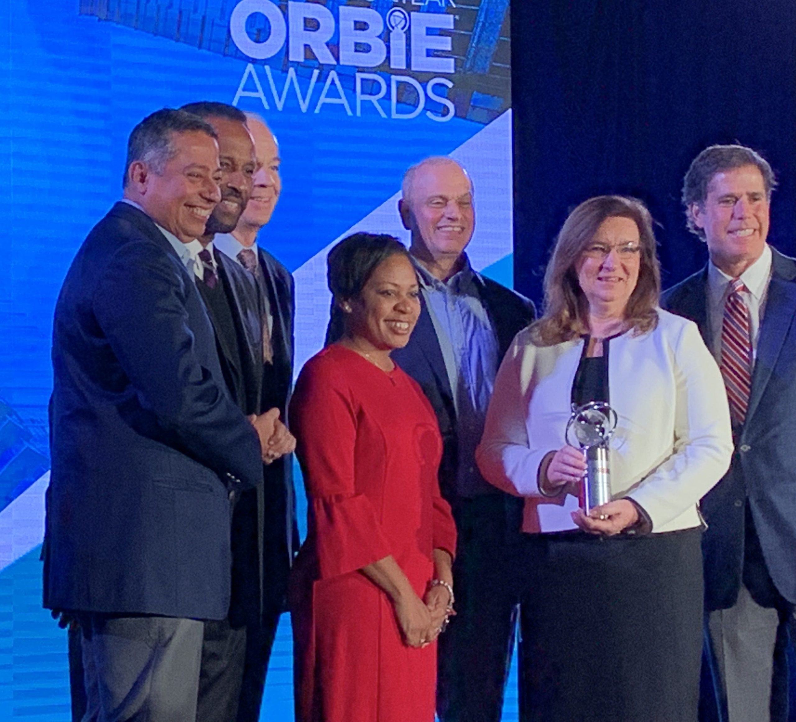 Shirl Stroeing holding her ORBIE award. She is surrounded by smiling colleagues.