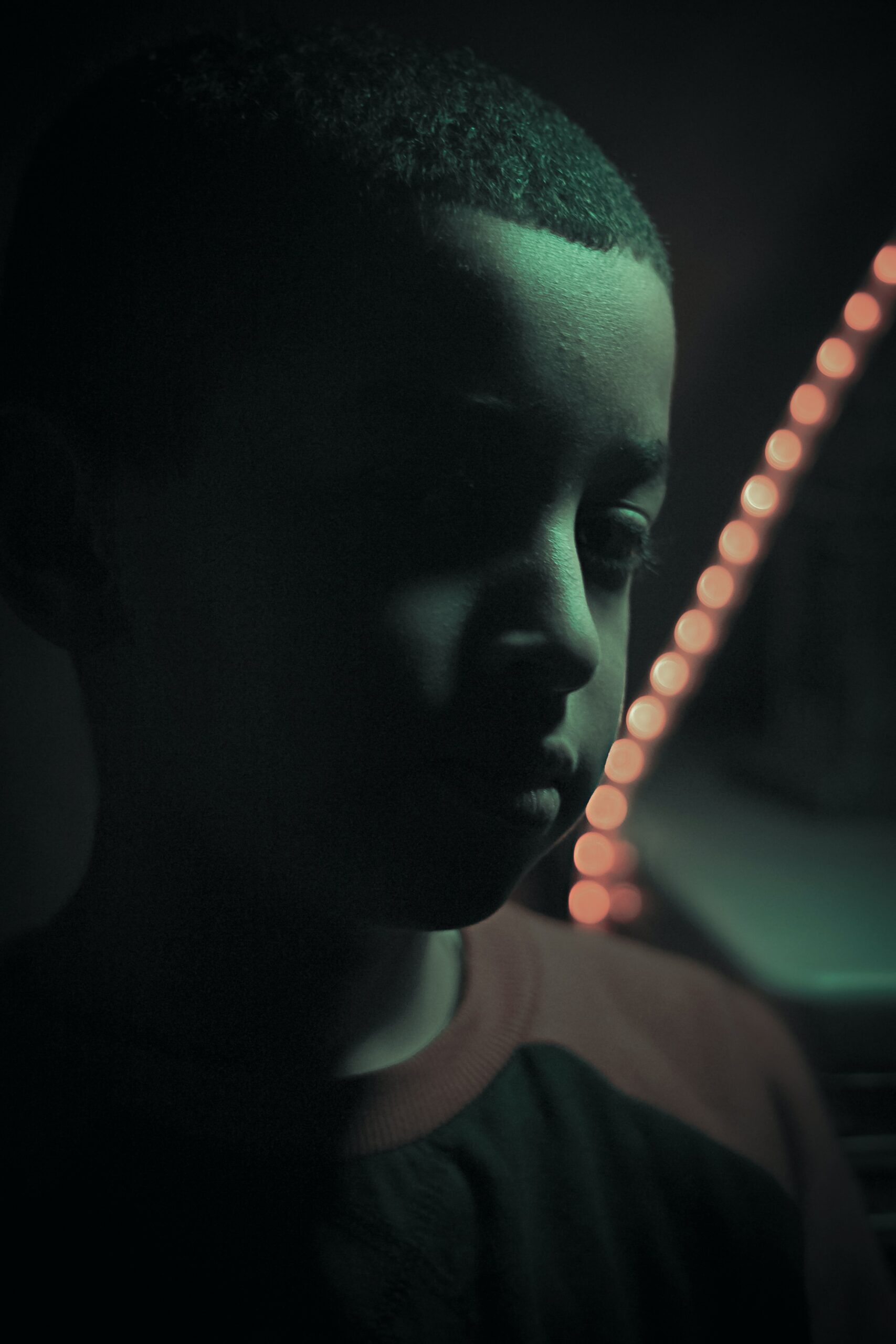 Stock photography closeup of sad boy in dim light; a string of out-of-focus lights appears behind him.