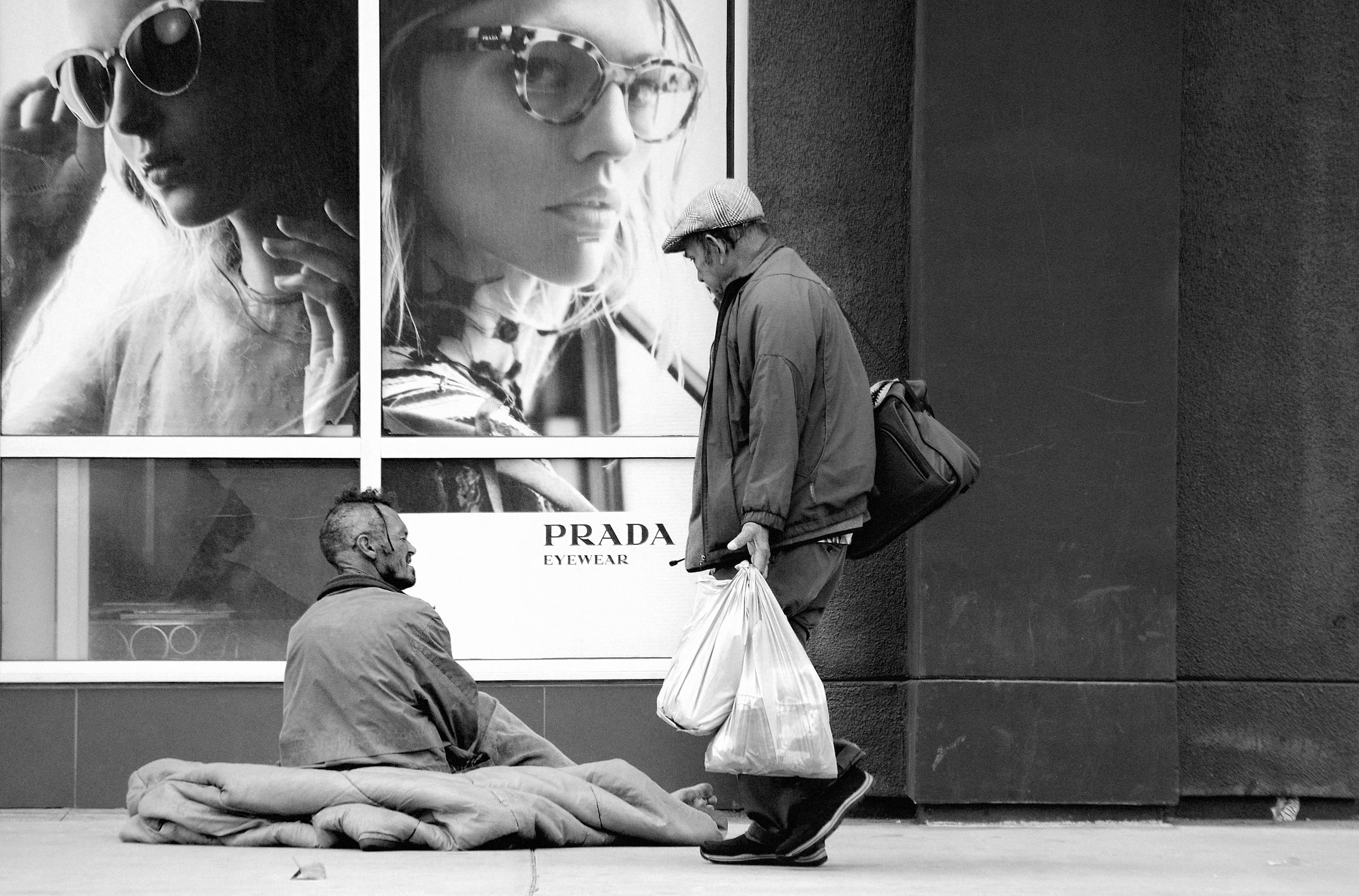 An unhoused man camps on the sidewalk in front of a Prada store in Los Angeles.