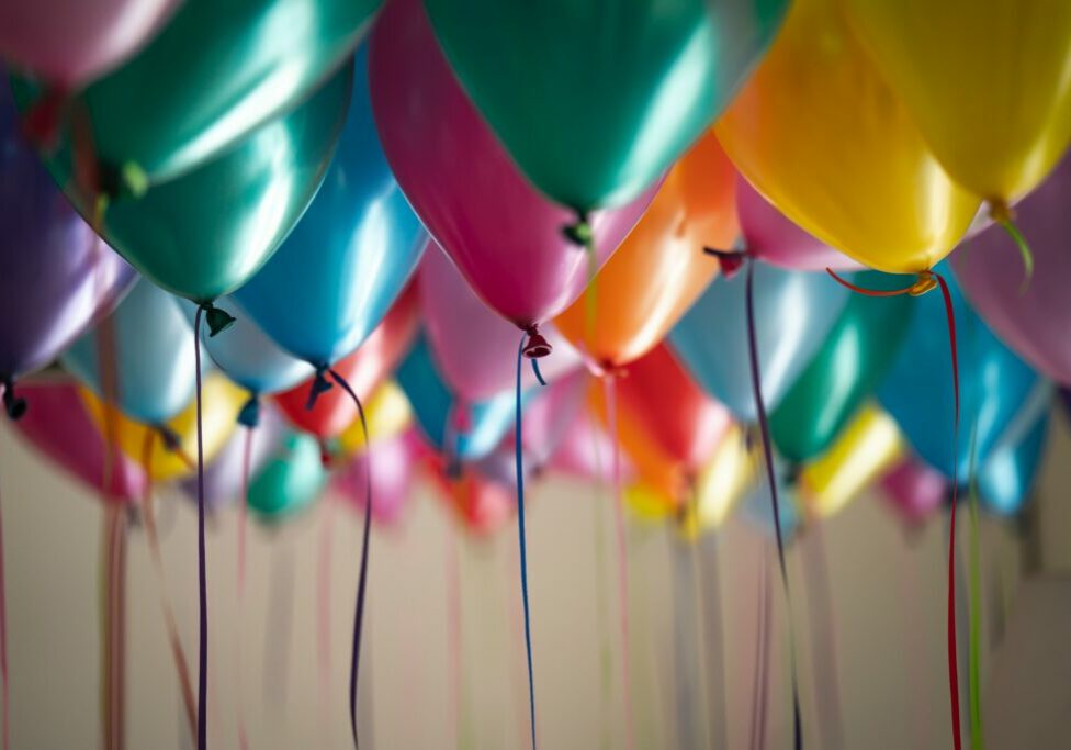 Colorful balloon arranged in rows with shallow depth of field. The balloons have colorful ribbons hanging from them.