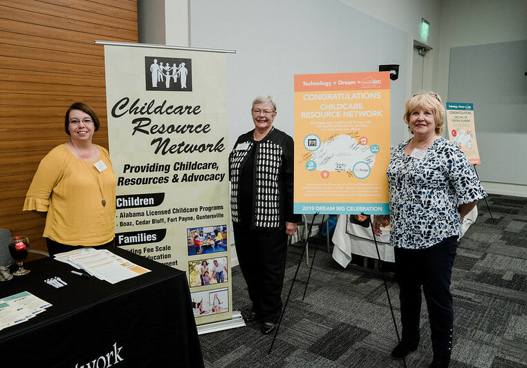 3 Child Resource Network (CRN) volunteers in front of CRN posters.