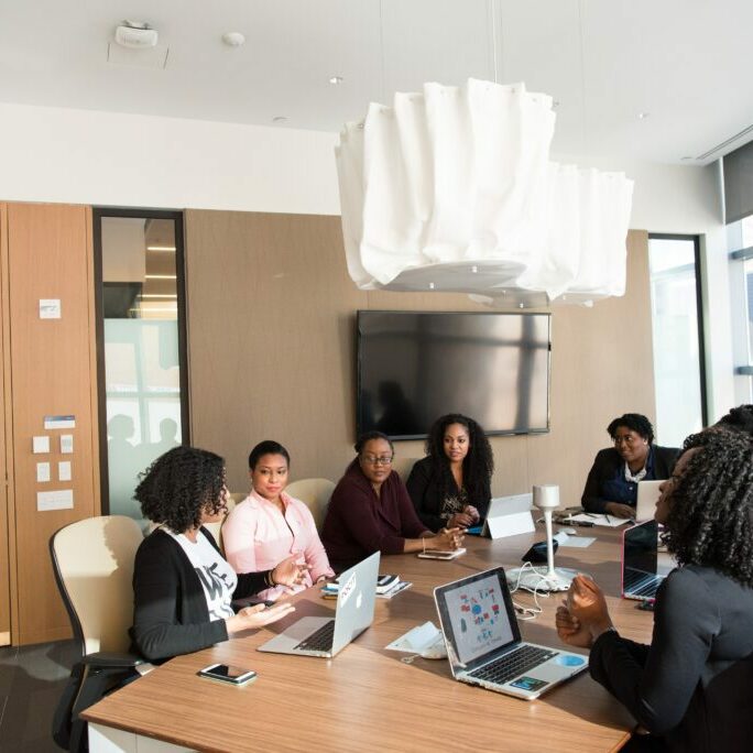 Black professional women in seated at a long table in a conference room\